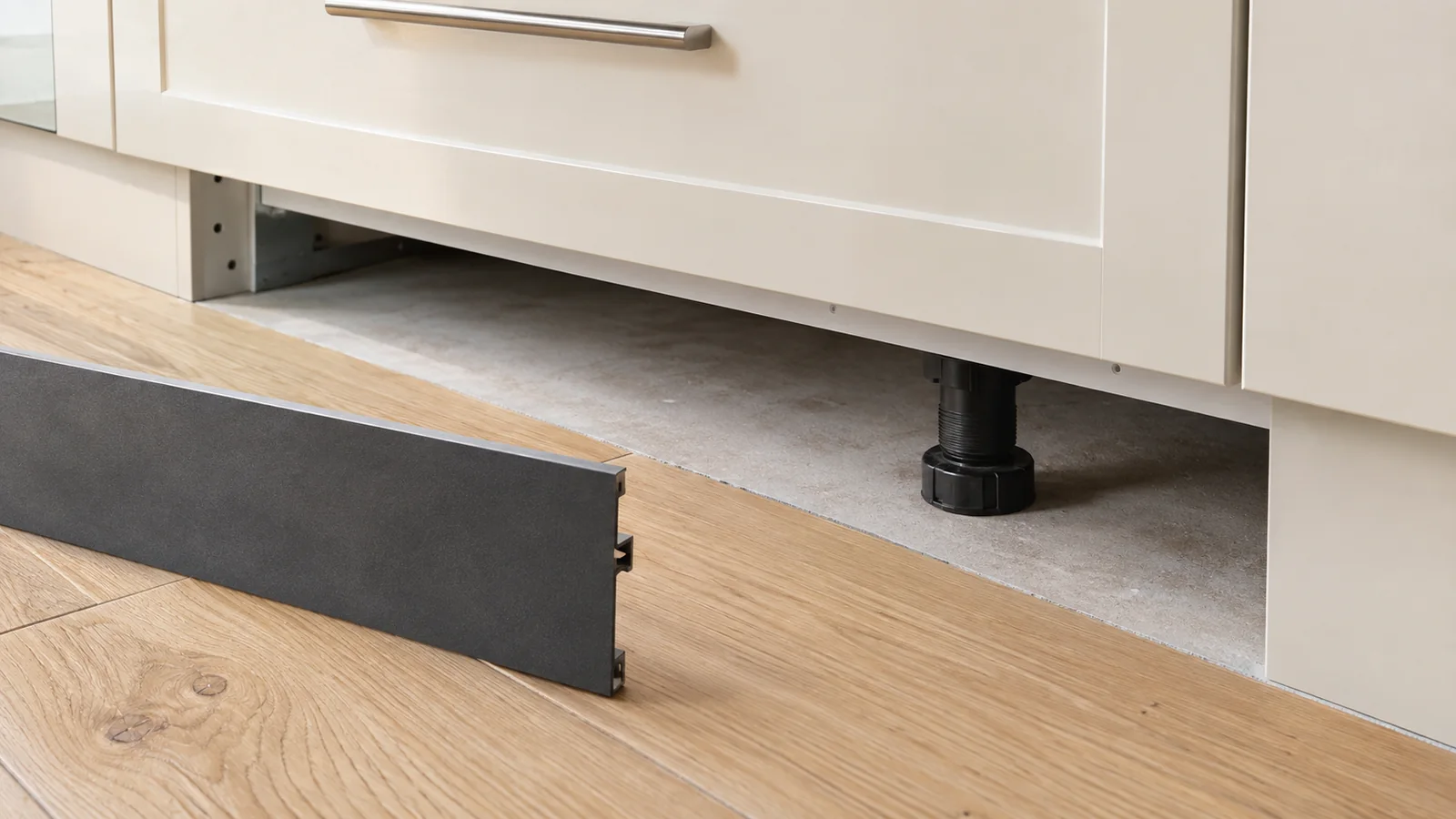 Cabinet base with a removable plinth set aside, showing a support foot and the edge of nearby plank flooring.